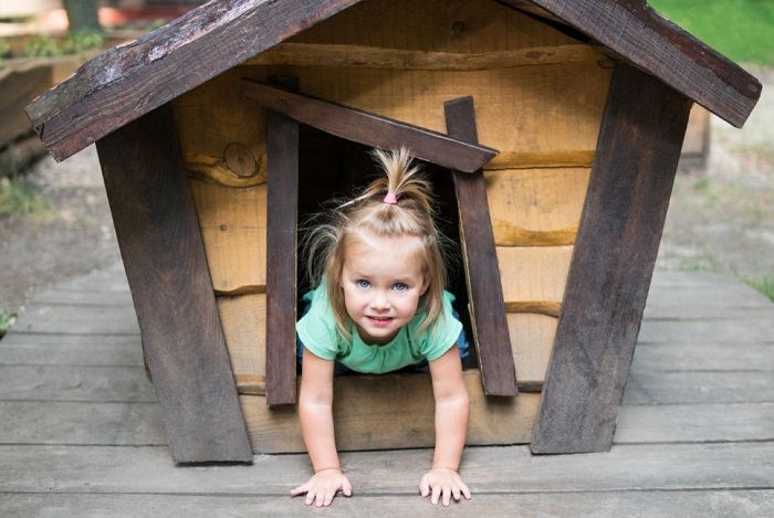 Een kind zit bij de ingang van een hondenhok.