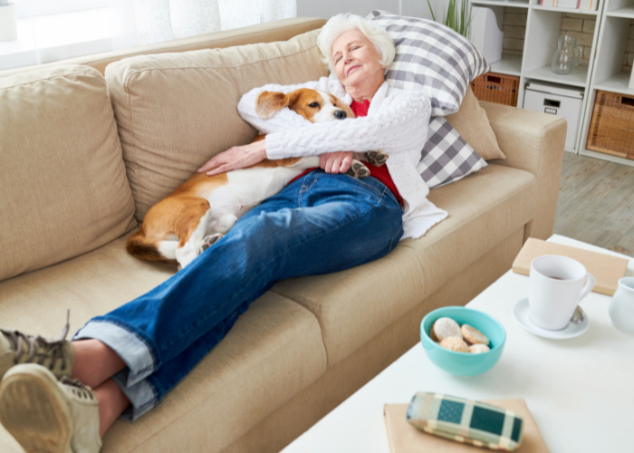 Een oudere vrouw ligt met haar hond op de bank.